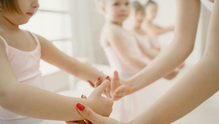 a little girl in a pink dress teacher showing girl how to hold her handsand