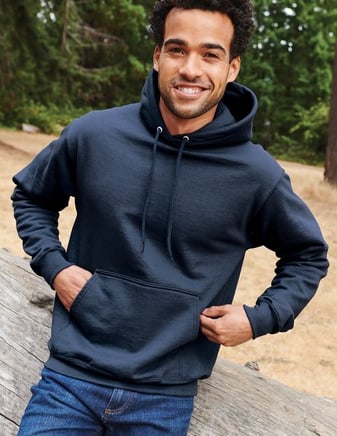 a man in a blue hoodie and jeans standing in front of a log cabin