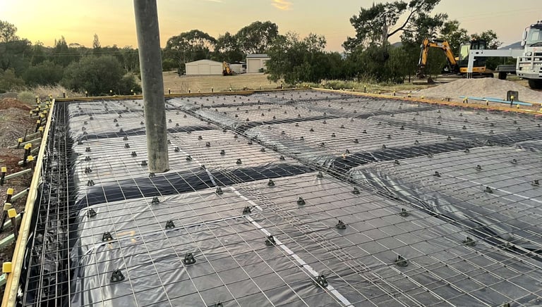 Concrete slab foundation under construction with steel reinforcement mesh and vapor barrier at sunset.