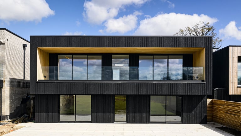 Modern two-story black timber-clad house featuring glass balconies and large windows.