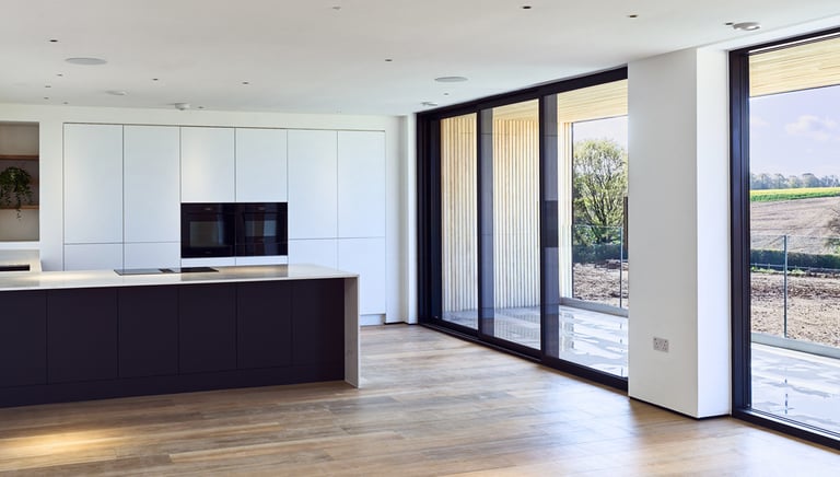 Modern minimalist kitchen with a black island, white cabinets, and large sliding glass doors.