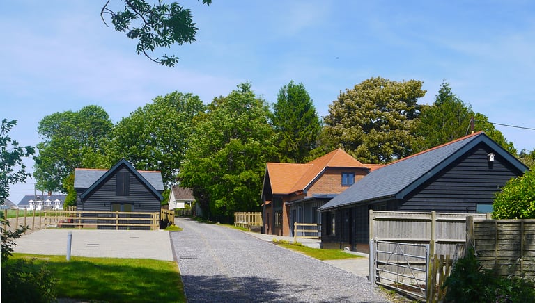 Modern black timber barn conversion cottages along a gravel driveway in a rural countryside setting.