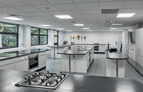 Modern teaching kitchen with stainless steel appliances and black countertops.