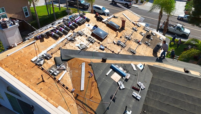 Aerial view of roofing contractors installing new asphalt shingles and underlayment on a residential home roof.
