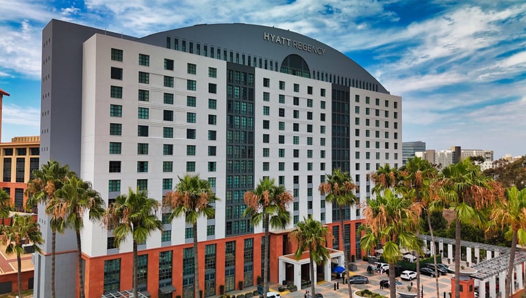 Exterior view of the Hyatt Regency hotel building with palm trees and a blue sky with white clouds.