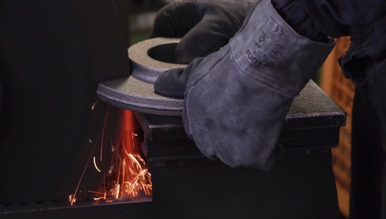 Gloved worker grinding a metal industrial part on a wheel with sparks flying.