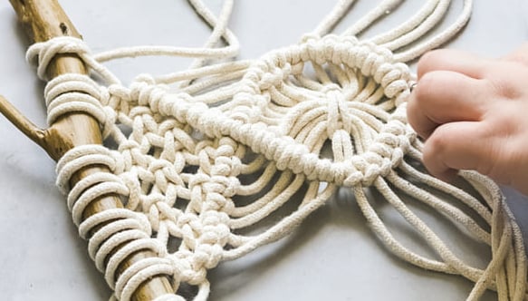 proyecto pequeño de macrame en blanco sobre un tronco de madera