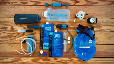 Backpacking water filters and gravity purification systems laid out on a wooden deck.