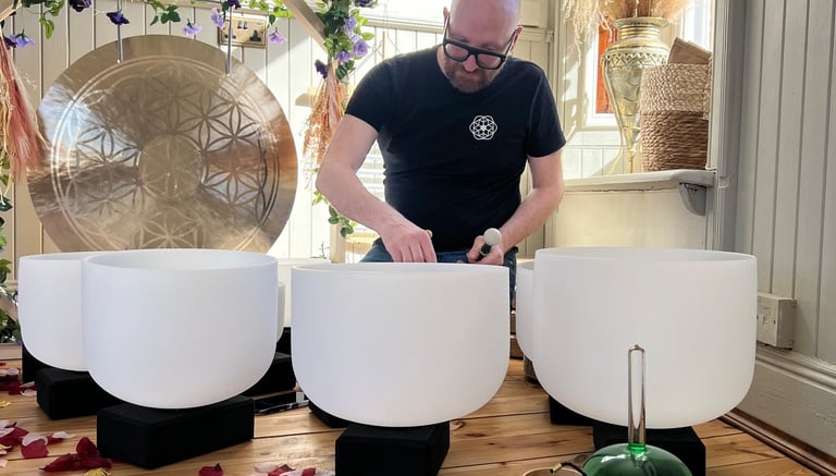a man sitting on a wooden floor with crystal signing bowls 