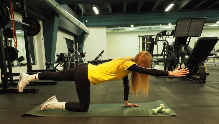Una donna in maglia gialla esegue un esercizio di equilibrio in ginocchio, estendendo il braccio e la gamba opposti,