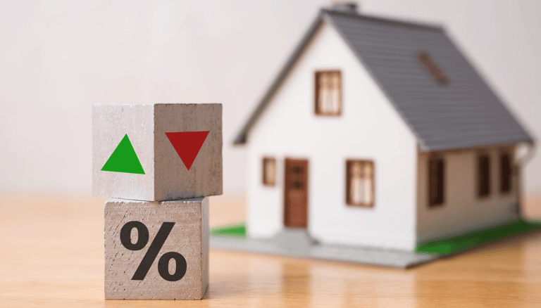 blocks with green and red arrows for interest rates beside tiny house