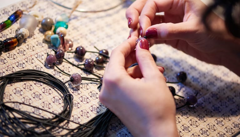 Joyera insetando cuentas de vidrio hechas a mano en un cordón negro para crear joyas personalizadas.