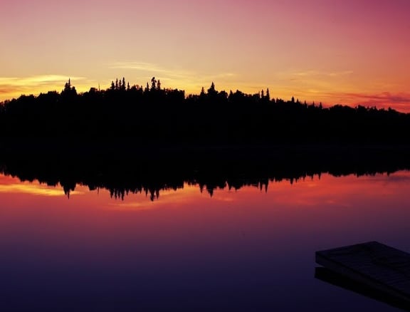 photo: reflection of fiery sunset and trees on a placid lake in Alaska