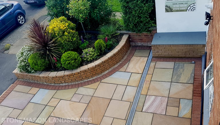 Colourful sandstone paving driveway and curved raised planter with colourful plants and flowers