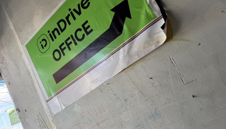 Green and white inDrive OFFICE directional sign with a black arrow on a grey concrete wall.