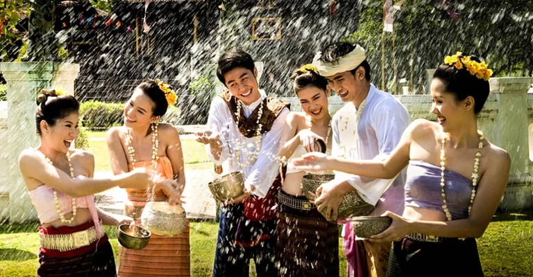Smiling group in traditional Thai clothing splashing water during Songkran festival celebration.