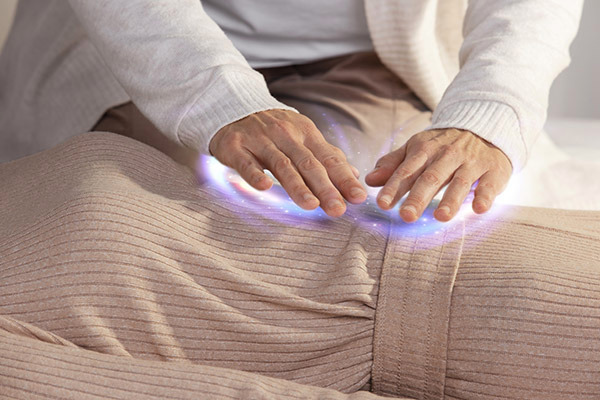 Person's hands hovering over another person, emitting a glowing light, during energy healing.