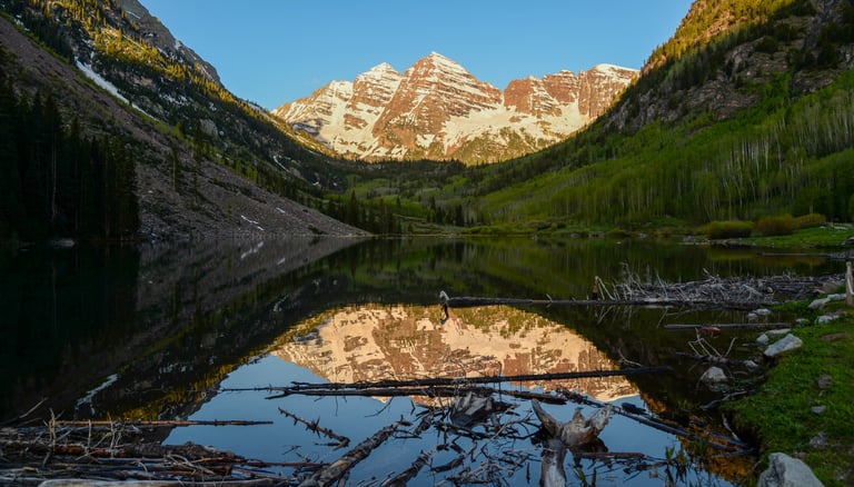 Spectacular Maroon Bells shine in the light of a summer sunrise with reflection in Maroon Lake