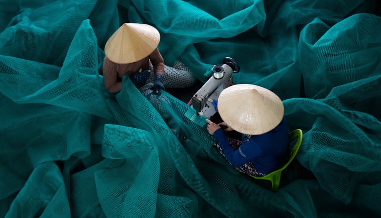 Two women wearing traditional Vietnamese conical hats repairing a fishing net.