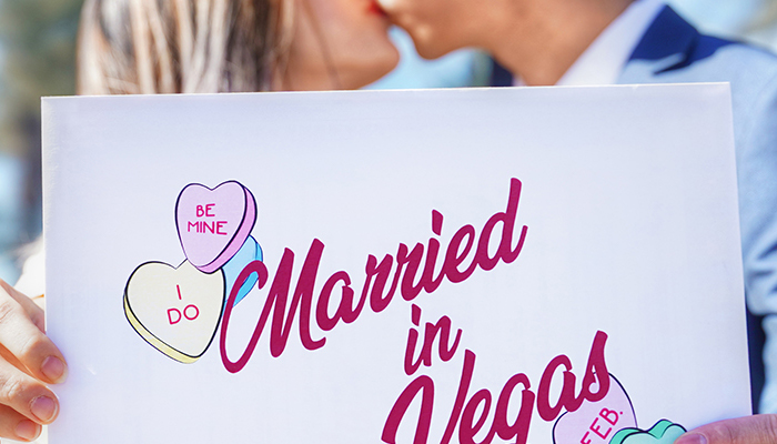 a man and woman kissing in front of a married in vegas sign