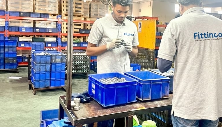 Factory workers at Fittinco inspecting high-quality hydraulic hose fittings in a manufacturing warehouse.