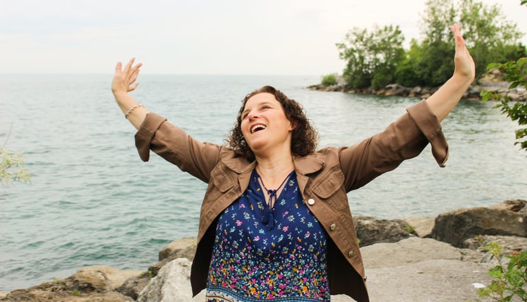 Natanya celebrating with hands in the air, lake behind