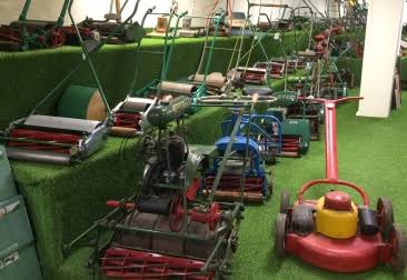 Collection of vintage lawn mowers displayed on artificial turf in a garden equipment museum.