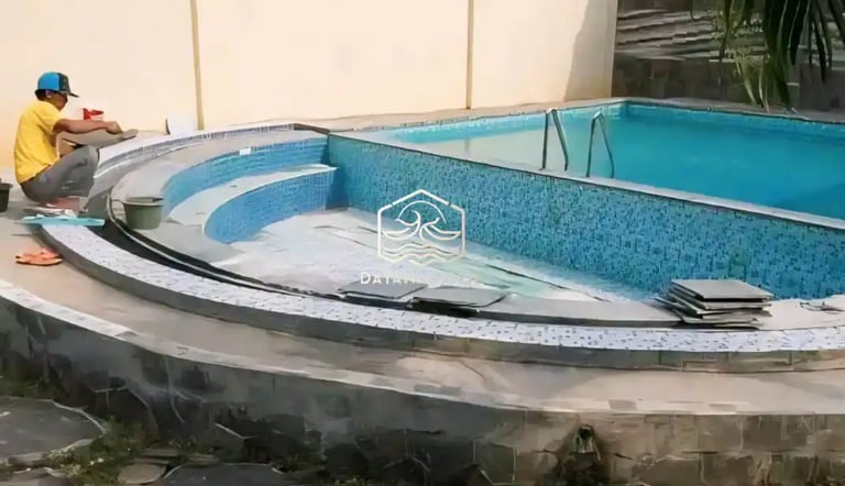 Proses pemasangan material finishing mozaik pada dinding kolam renang oleh tukang berpengalaman.