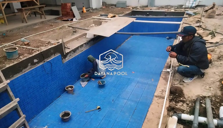 Proses pemasangan material finishing mozaik pada dinding kolam renang oleh tukang berpengalaman.