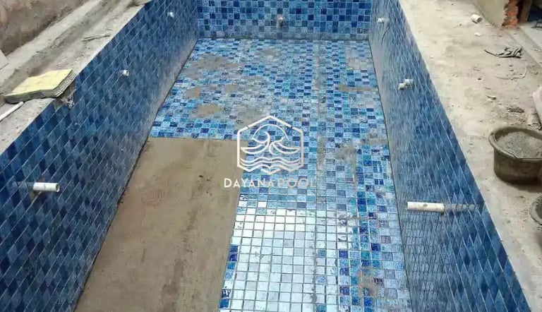 Proses pemasangan material finishing mozaik pada dinding kolam renang oleh tukang berpengalaman.
