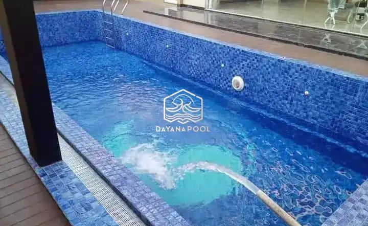 Proses pemasangan material finishing mozaik pada dinding kolam renang oleh tukang berpengalaman.