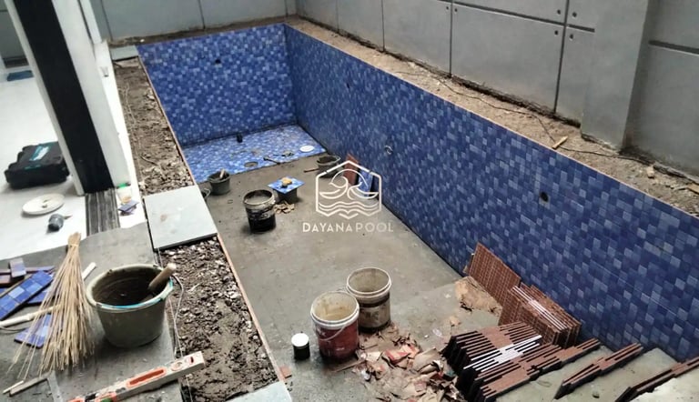 Proses pemasangan material finishing mozaik pada dinding kolam renang oleh tukang berpengalaman.