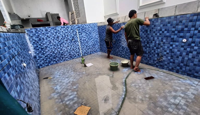 Proses pemasangan material finishing mozaik pada dinding kolam renang oleh tukang berpengalaman.