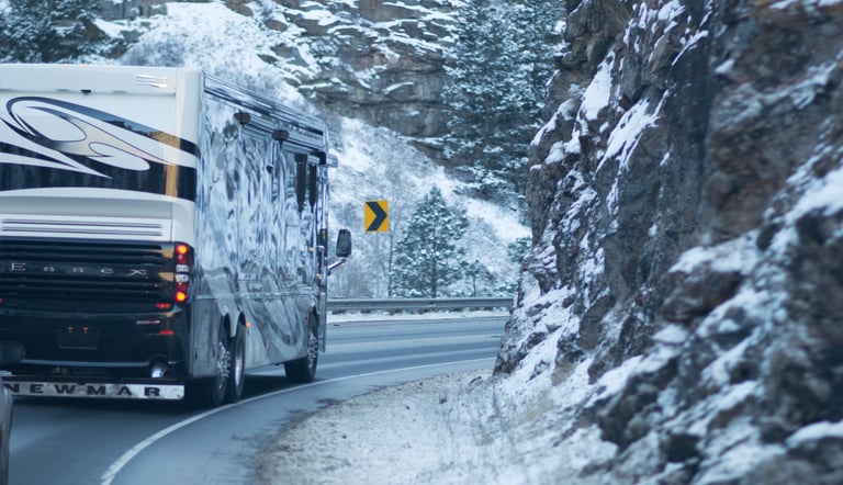 A luxury Newmar Essex motorhome RV driving on a winding snowy mountain road.