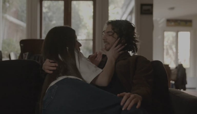 A young couple embracing each other and smiling, while relaxing on a sofa in a living room.