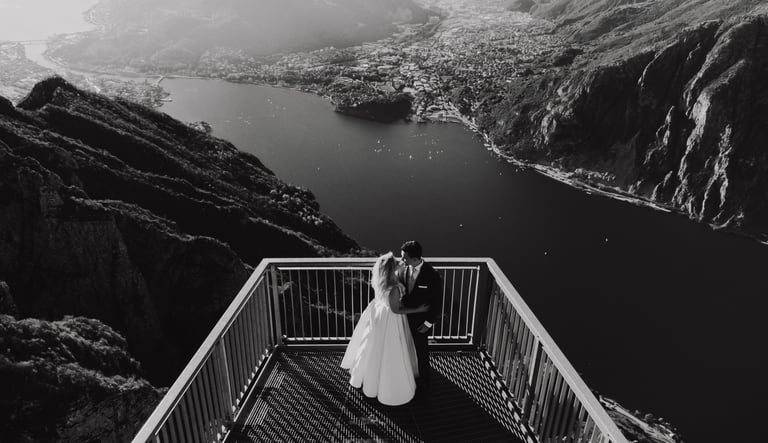a bride and groom standing on a balcony railing overlooking a mountain