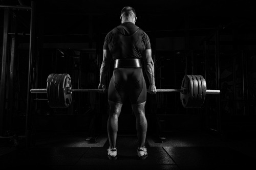 Rear view of a bodybuilder performing a heavy barbell deadlift in a dark gym.