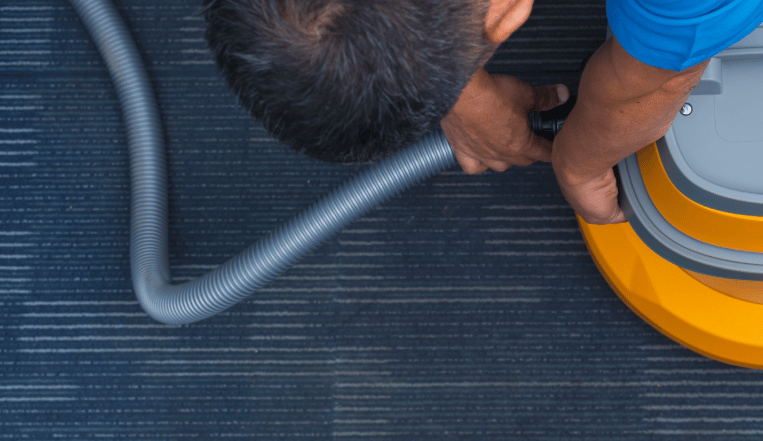 a man in a blue shirt connecting a hose to a carpet cleaning machine 