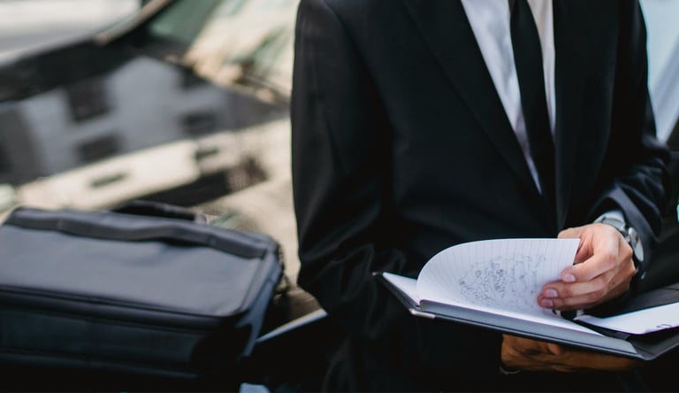 Un professionnel assis sur le capot d’une voiture, en train de prendre des notes sur un carnet.