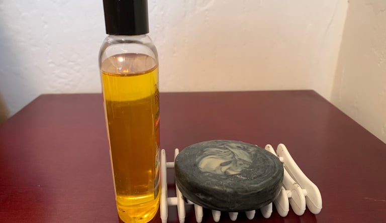 A bottle of golden colored oil next to a bar of round black soap