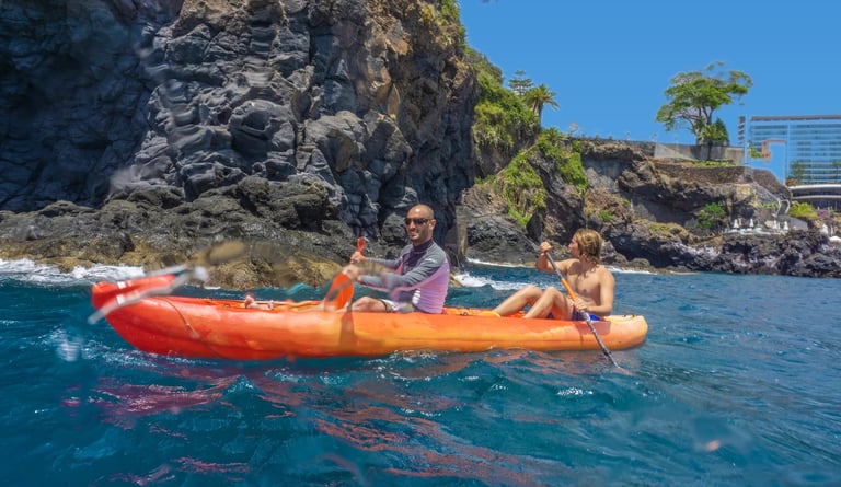 Guide and guest paddling an orange tandem kayak along the rocky volcanic cliffs of Funchal, Madeira