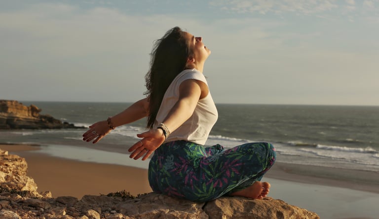 jeune femme assise en tailleur en haut d'une falaise avec la mer en fond