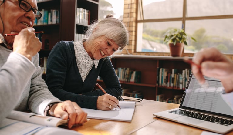 Personas mayores realizando ejercicios de estimulación cognitiva en grupo, escribiendo en cuadernos 
