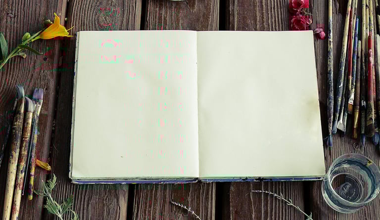 Libro abierto sobre mesa de madera, rodeado de pinceles y flores. En Cerebro Nostrum ofrecemos libro