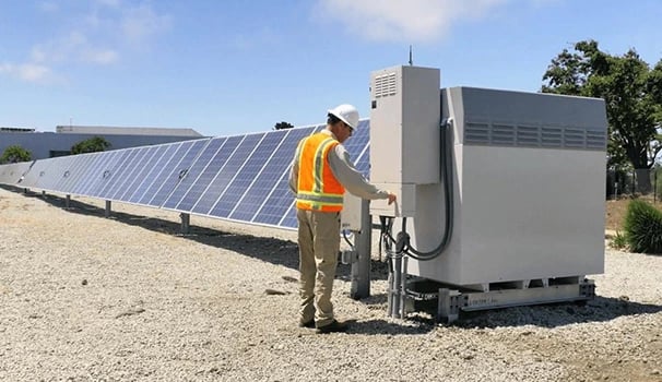 A technician inspecting solar panels and an inverter system at a renewable energy farm.