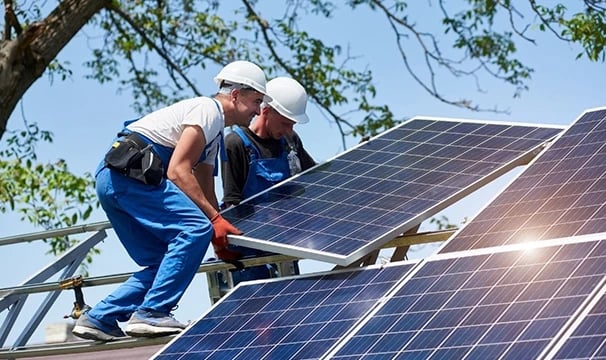 Professional solar installers in hard hats mounting photovoltaic panels on a residential rooftop.