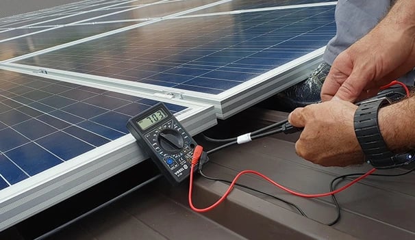 Technician using a digital multimeter to test the voltage of solar panels on a rooftop installation.