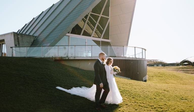 Bride and groom walking down a hill, wedding venue in the background, Canberra wedding photographer