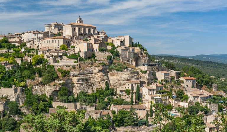 Panoramic view of the hilltop village of Gordes in Provence, France, featuring historic stone buildings and cliffs.