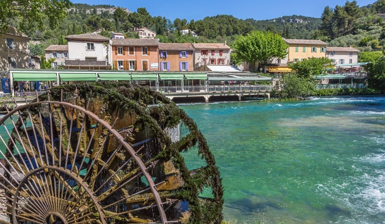 Historic mossy water wheel in Fontaine-de-Vaucluse by the turquoise Sorgue river in Provence, France.